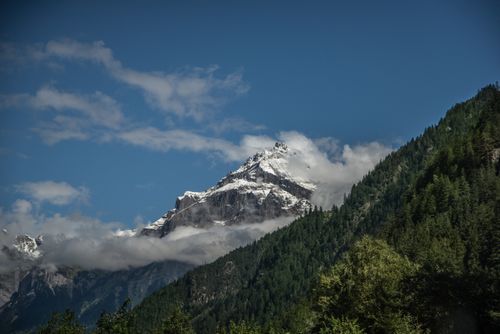 Free Stunning view of a snow-capped mountain peak surrounded by lush green forests under a clear blue sky. Stock Photo