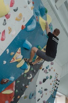Man engaged in indoor rock climbing on a vibrant, colorful wall for fitness and recreation.