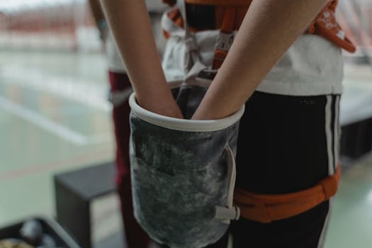 A rock climber prepares for climbing with chalk bag and harness in an indoor gym setting.