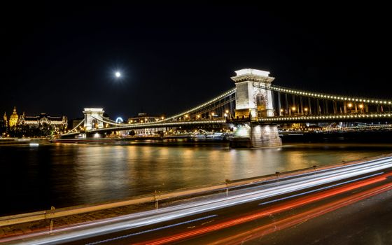 布达佩斯链桥的夜景中，光线条纹和满月倒映在多瑙河上