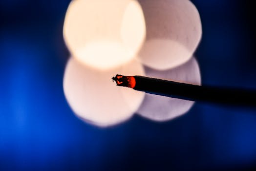 Close-up of a burning incense stick against a vibrant bokeh background.