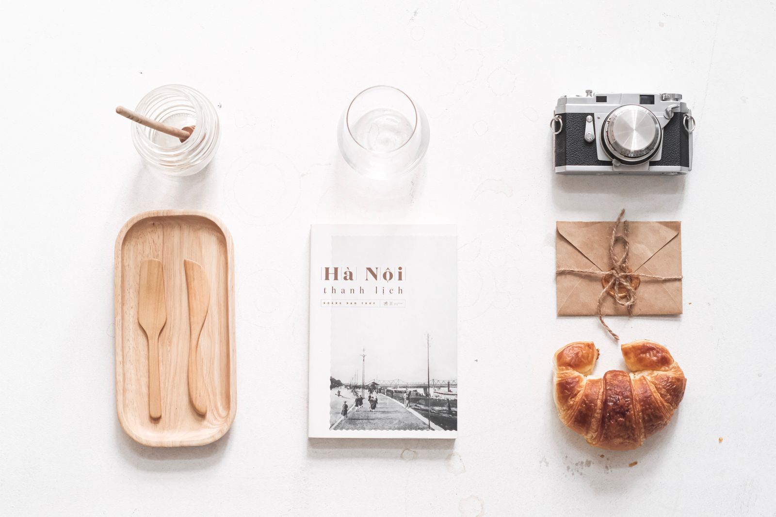 Vintage flat lay with a camera, croissant, and Hà Nội book on a white background.