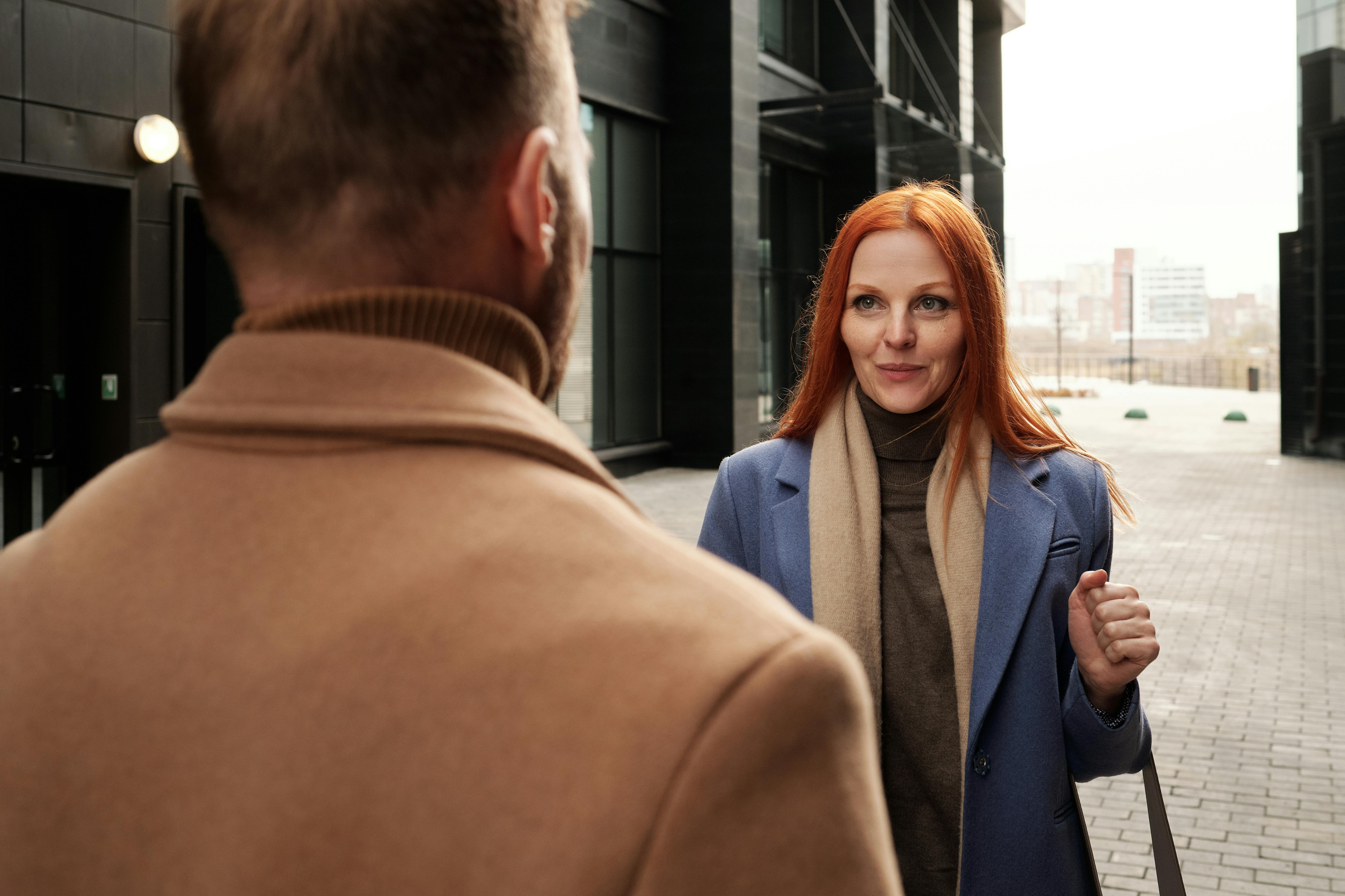 a woman wearing a blue coat talking to a man