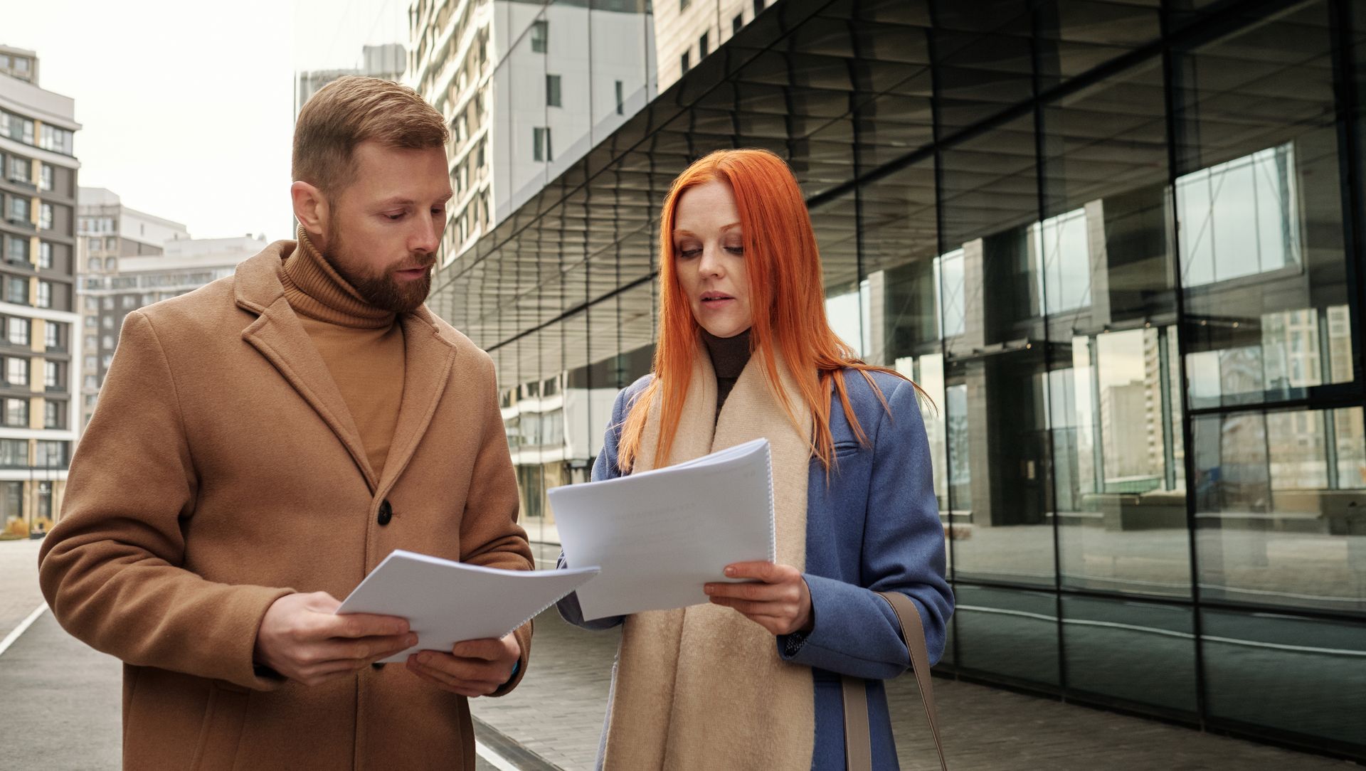 Two business professionals in urban setting reviewing documents together.