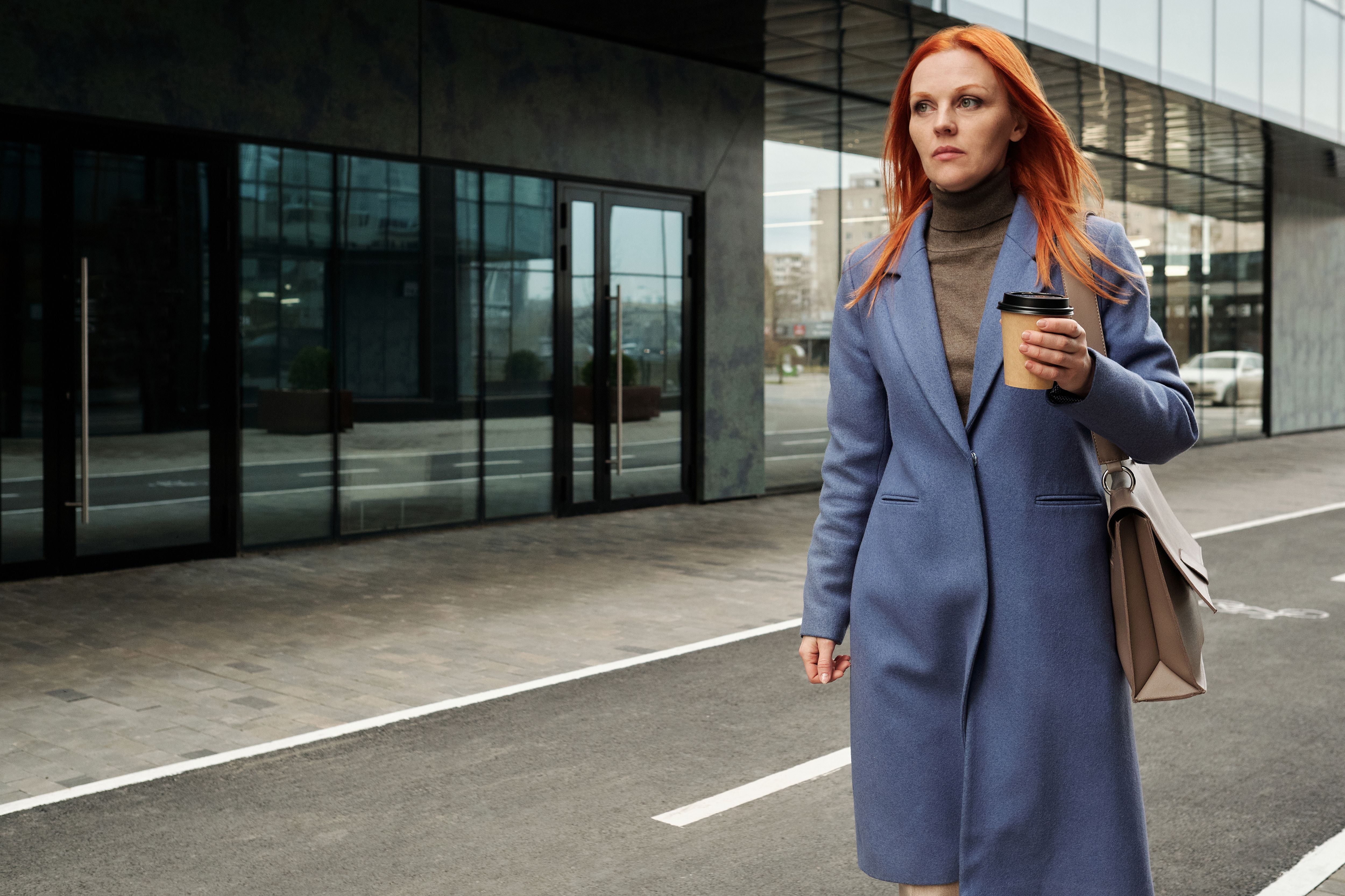 一位穿着蓝色外套的女商人，手拿咖啡走在外面，散发着自信
