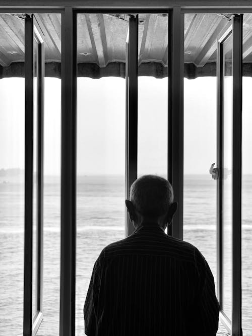 Free Back View of an Elderly Man Staring at the Sea Stock Photo