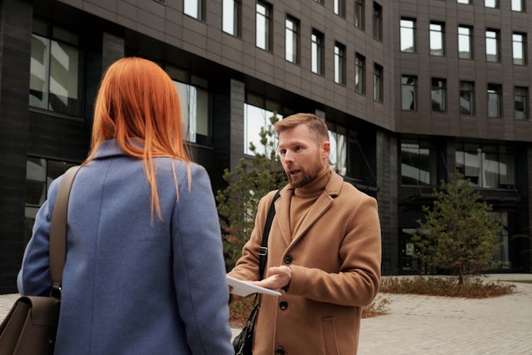 Redhead Man And Woman Talking By A Gray Office Building