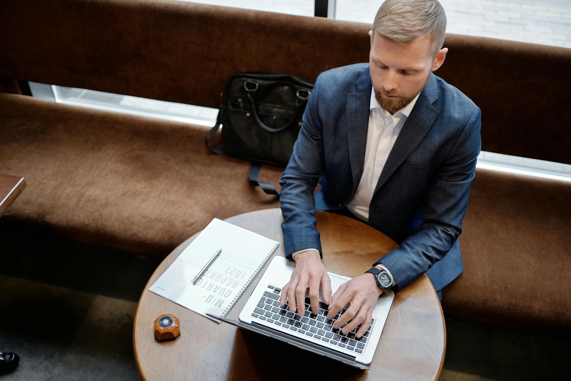 Overhead view of a man in a suit typing on a laptop at a round table.