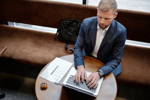 Free Overhead view of a man in a suit typing on a laptop at a round table. Stock Photo