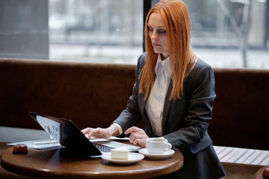 A businesswoman in a suit typing on a laptop while seated in a cozy cafe.