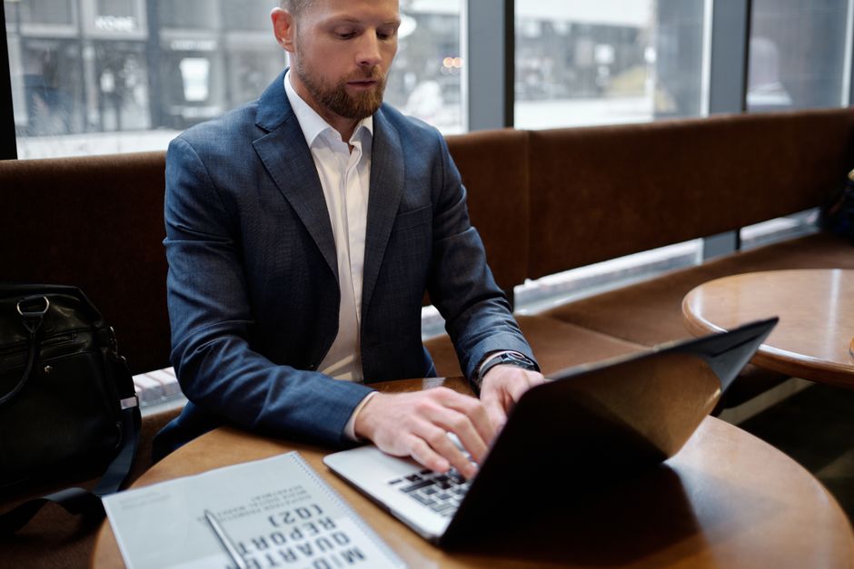 Um empresário profissional em um terno trabalhando em um laptop em um café, focando em um relatório.