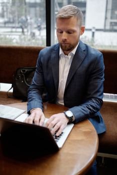 Focused businessman typing on a laptop indoors, showcasing modern work environment.