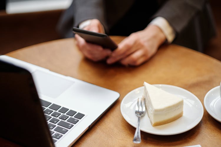 Close-up Of Cake And Laptop While Using Smartphone