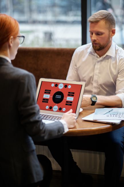 A professional man and woman discussing business strategies using laptops in an indoor setting.