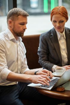 Two professionals collaborating on a laptop in a modern cafe setting.