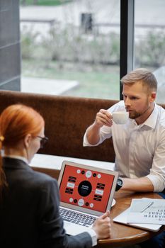 Business professionals discussing over coffee in a cafe setting with a laptop.