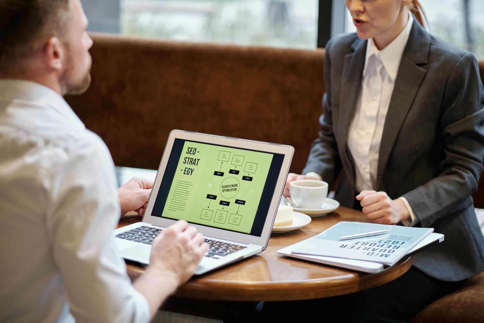 A man and woman engaged in a business meeting discussing SEO strategy in a cozy cafe setting.