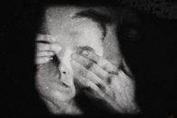 Black and white of anonymous serious person covering eyes with hands against black background