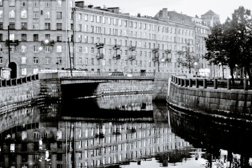 Black and white of residential buildings placed near calm river channel in city in daytime