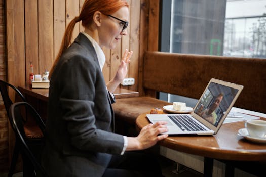 Businesswoman waving during an online meeting in a cozy café setting.