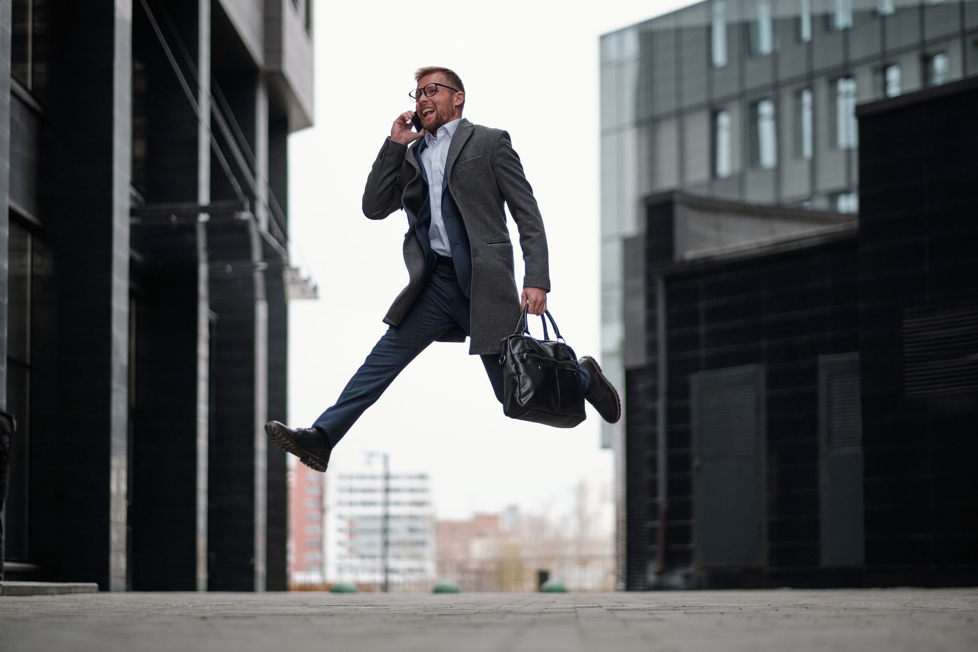 Dynamic businessman jumping while talking on phone in a modern cityscape.