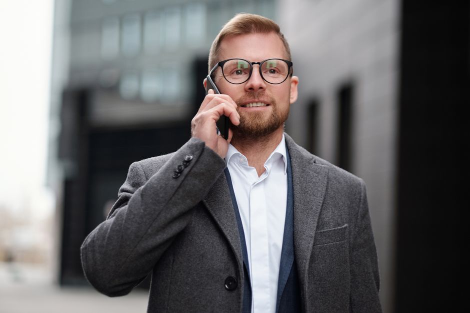Professional man in a gray coat making a phone call outside in an urban setting.