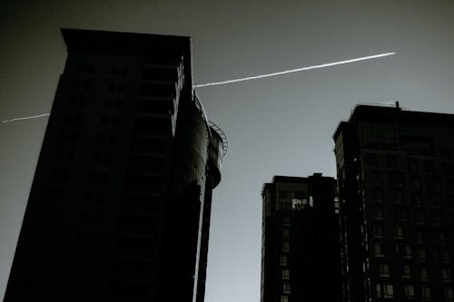 Free From below of  black and white apartment buildings in city district on background of cloudless sky with airplane trace Stock Photo