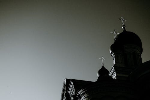 Low angle black and white of old stone temple exterior with crosses on domes under gray sky in city