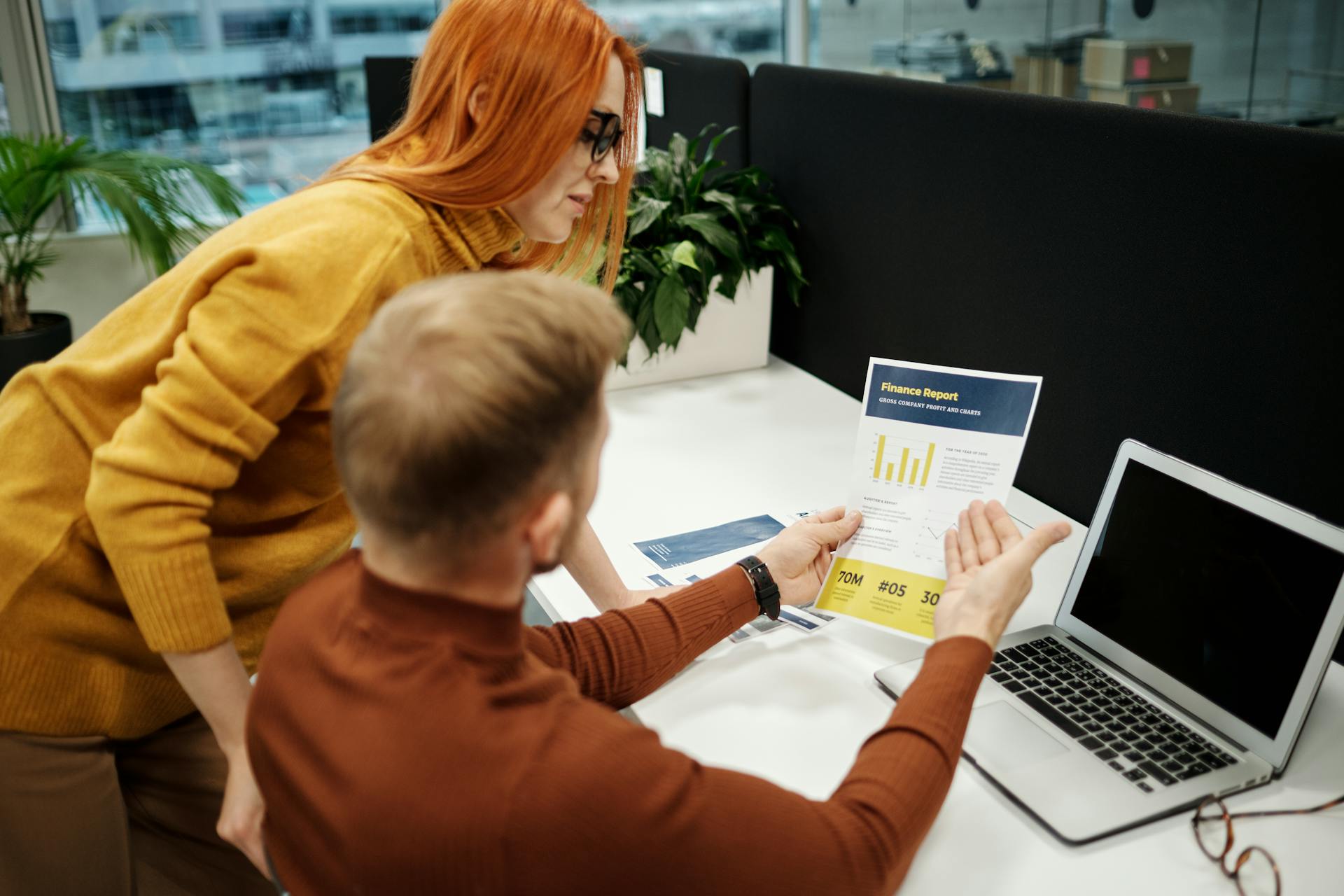 Two colleagues analyzing a financial report in a modern office setting with a laptop.