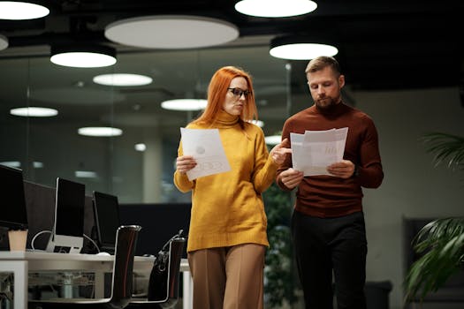 Two colleagues review documents while walking through a contemporary office space.