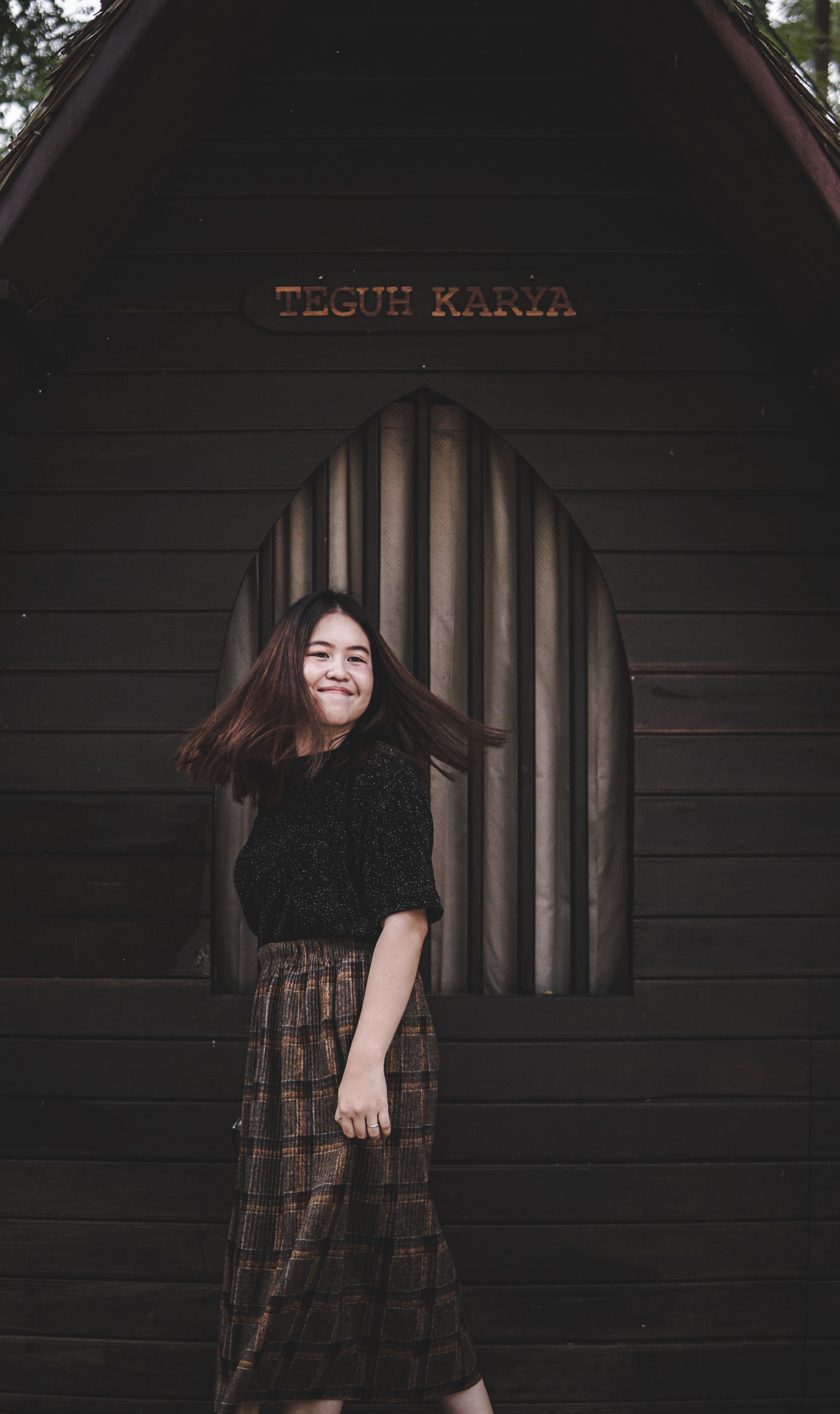 Joyful woman twirling in front of rustic wooden structure, embodying happiness and freedom.