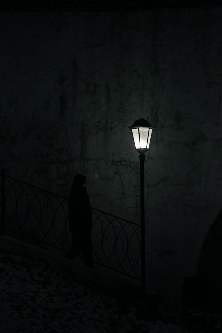 Silhouette Of Man Walking Near Bright Vintage Streetlight