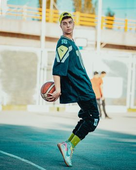 Stylish young man posing with a basketball outdoors in sunny Mashhad.
