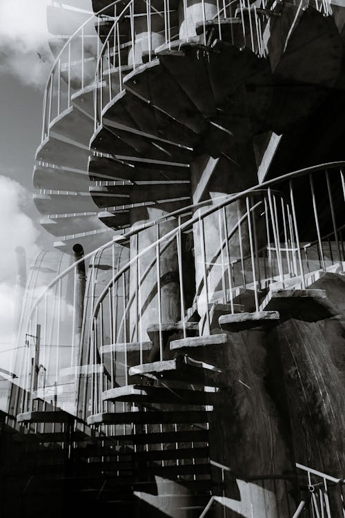 Black and white double exposure of tall stone spiral stairway with metal railings and pillar located on street in city