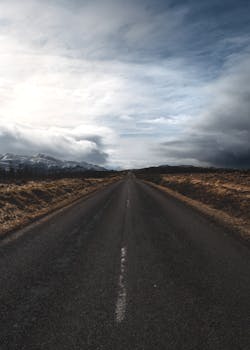 Lonely road stretching into distance under a dramatic cloudy sky, capturing a sense of solitude.