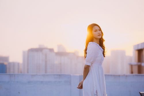 Free A serene portrait of an Asian woman embracing the golden hour on a city rooftop in Vietnam. Stock Photo