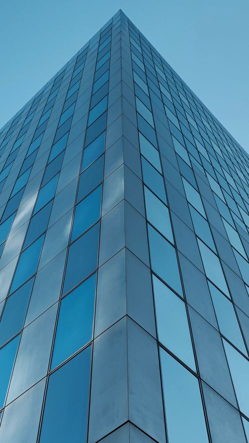Free Low angle shot of a sleek, glass-paneled skyscraper in Amsterdam, reflecting a clear blue sky. Stock Photo