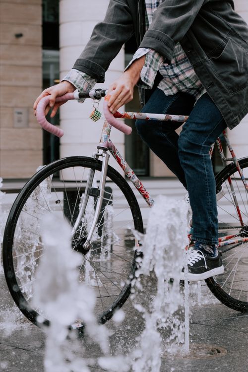 Free Cyclist rides through urban fountains, capturing a dynamic and refreshing street scene. Stock Photo