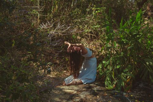 Free A woman dressed in white performs a yoga pose amidst vibrant green plants in a forest. Stock Photo