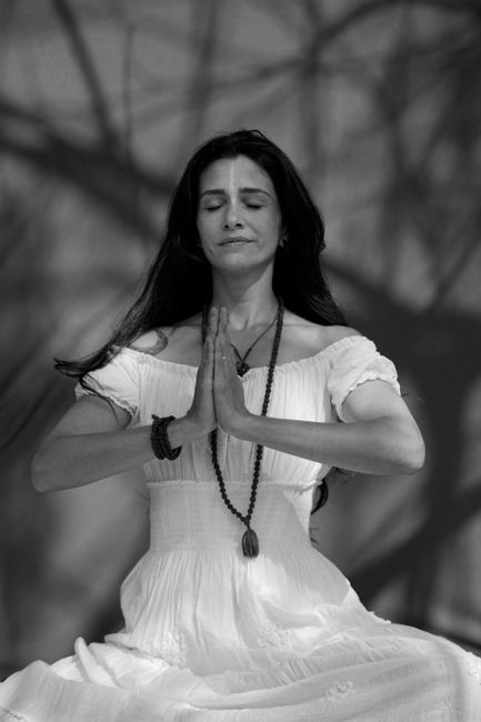 Black and white of tranquil female with closed eyes and folded hands meditating while sitting in forest on blurred background