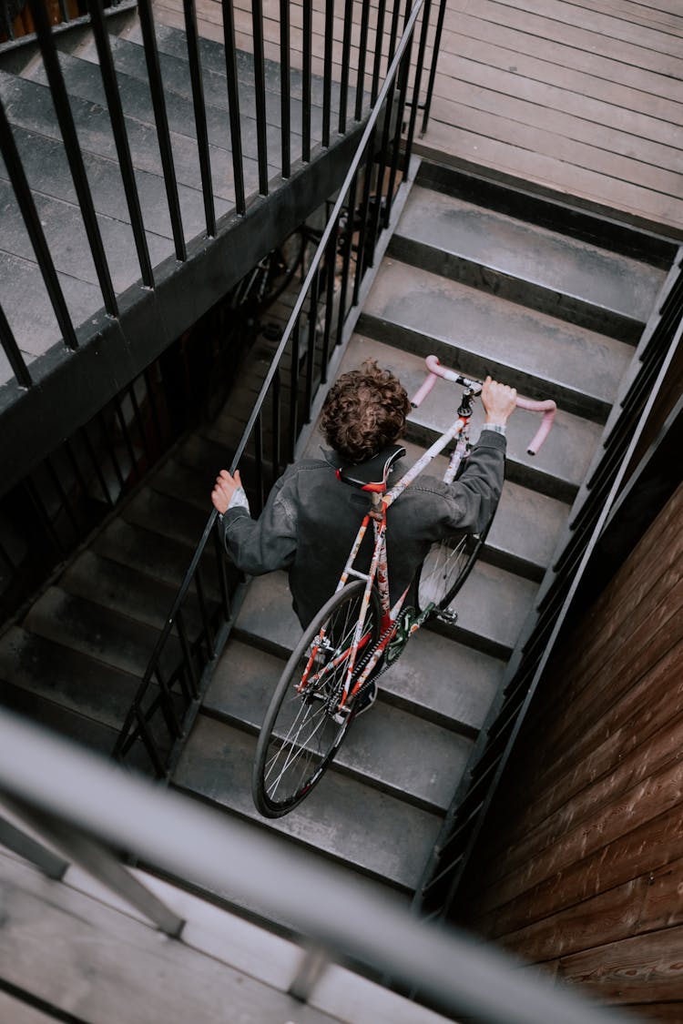 A Man Carrying A Bicycle While Walking Up A Wooden Staircase