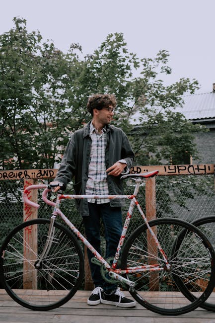 A young man standing with a fixie bike against a graffiti fence outdoors.