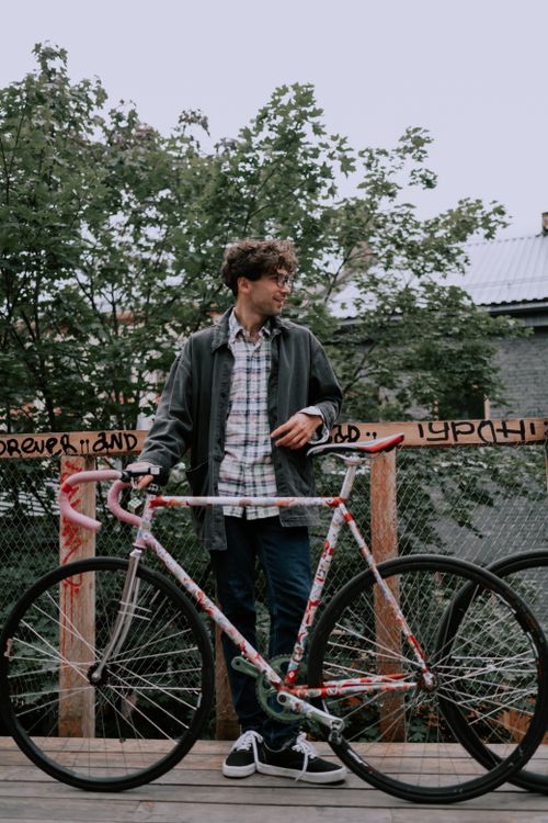 Free A young man standing with a fixie bike against a graffiti fence outdoors. Stock Photo