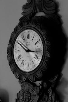 Black and white of round old fashioned clock with dial and curved ornamental details with retro design placed on blurred background