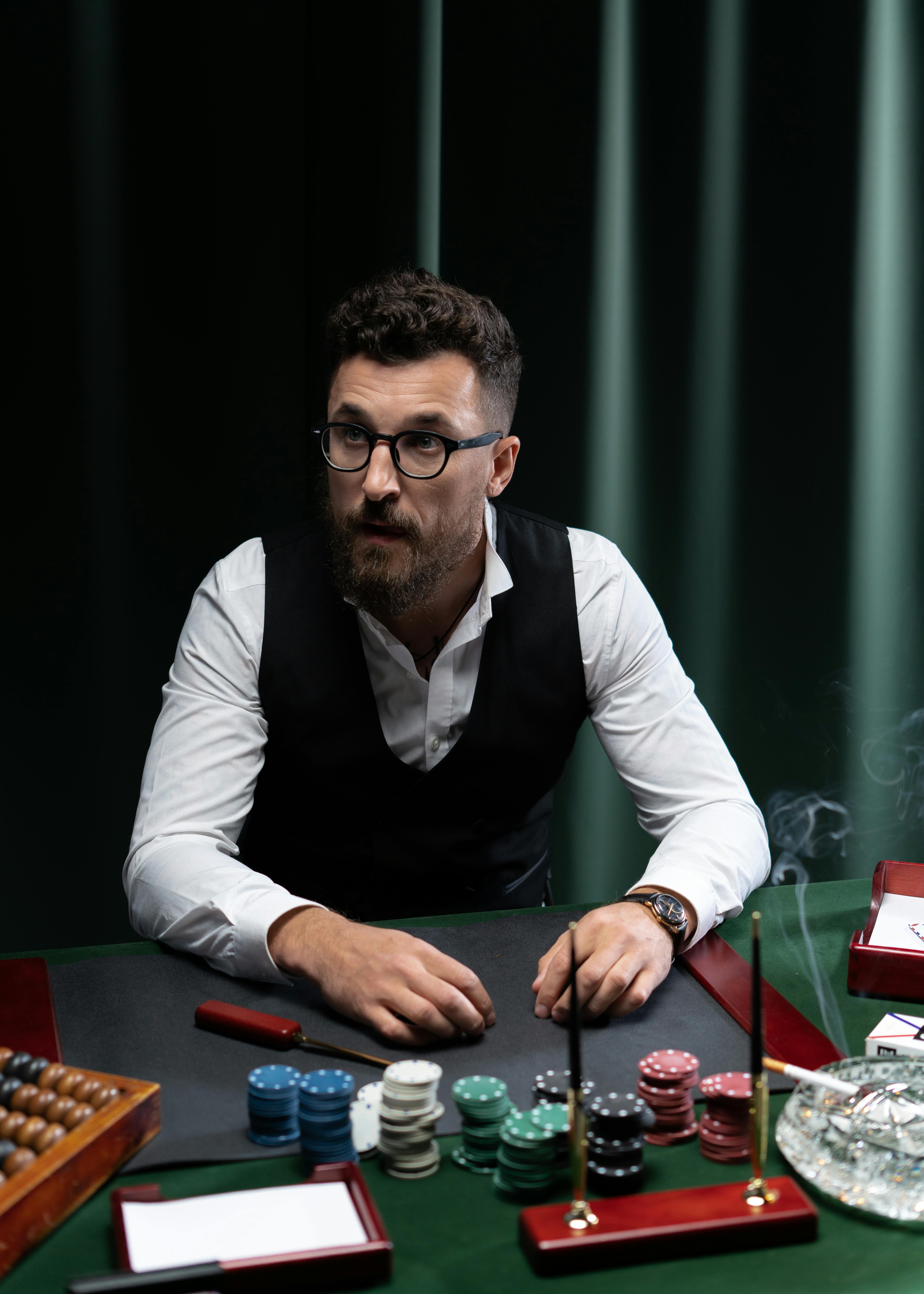 man in black vest seated on table with casino chips