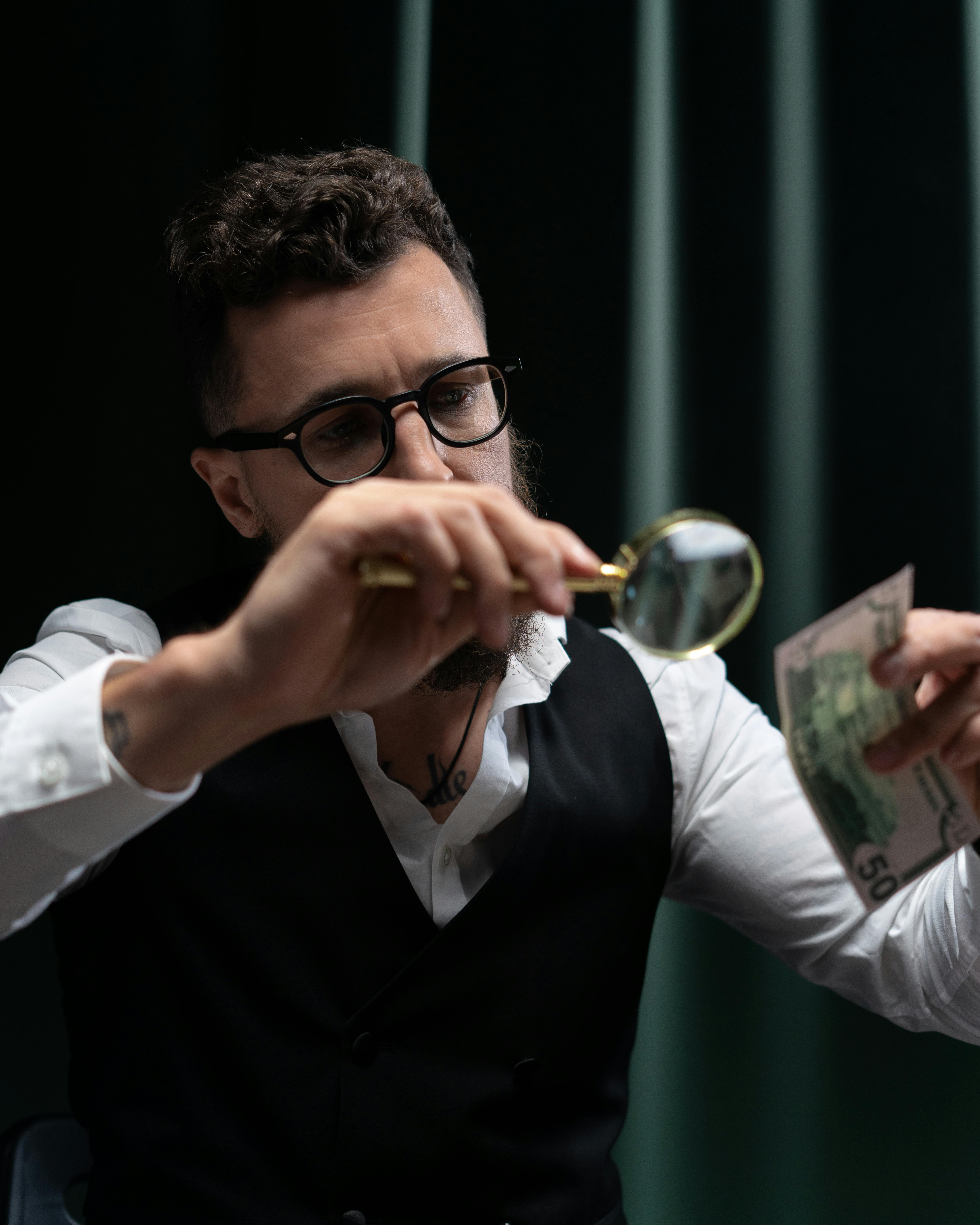 a man holding a magnifying glass scrutinizing cash money