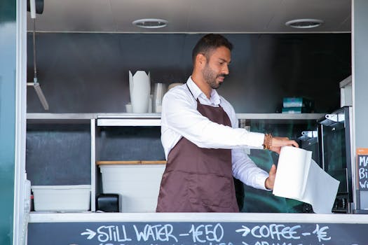 A barista in an apron prepares coffee in an outdoor food truck, exuding hospitality and professionalism.