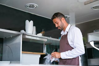 Side view of ethnic man putting on cellophane gloves while working in kitchen of cafe