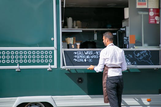 Back view of male seller wearing apron preparing food truck with menu written on board