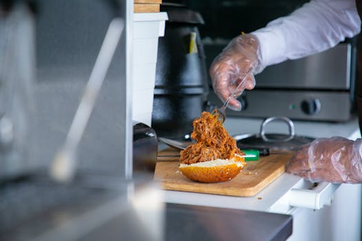 A chef uses gloves to prepare a delicious pulled pork sandwich in a professional kitchen.